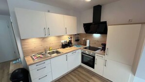 Een kleine keuken met witte kastjes, een houten aanrecht, een spoelbak, een kookplaat en een zwarte afzuigkap.