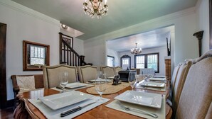 A dining area with a wooden table set for four, including white plates, cutlery, and wine glasses. - Heisman House - Book for football season!  Walk to Stadium! (Tuscaloosa)