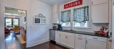 A kitchen with white cabinets, a black countertop, and a window with checkered curtains.