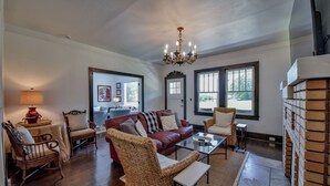 A spacious living room with a red leather sofa, wicker chairs, a glass coffee table, and a chandelier. - Heisman House - Book for football season!  Walk to Stadium! (Tuscaloosa)