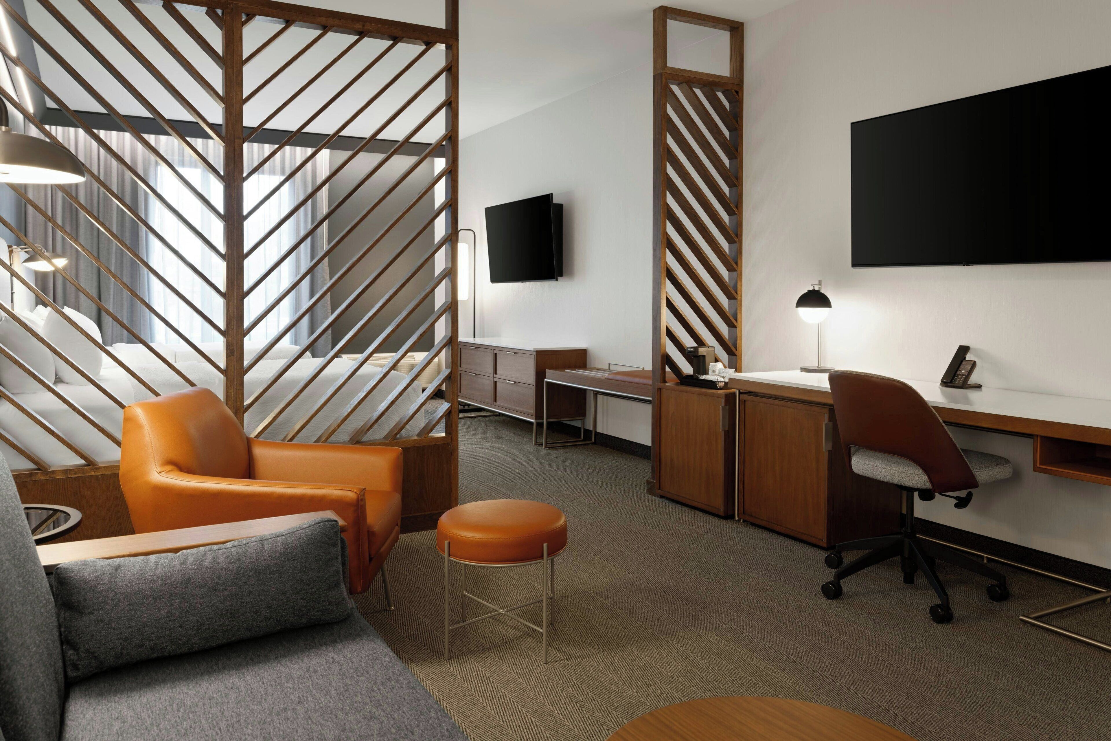 Una habitación de hotel moderna con un sofá, dos sillones, un escritorio y un televisor.