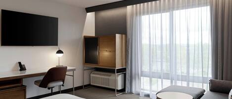 Habitación de hotel con cama, escritorio con silla, televisor, calefacción, sofá y una ventana grande con cortinas.