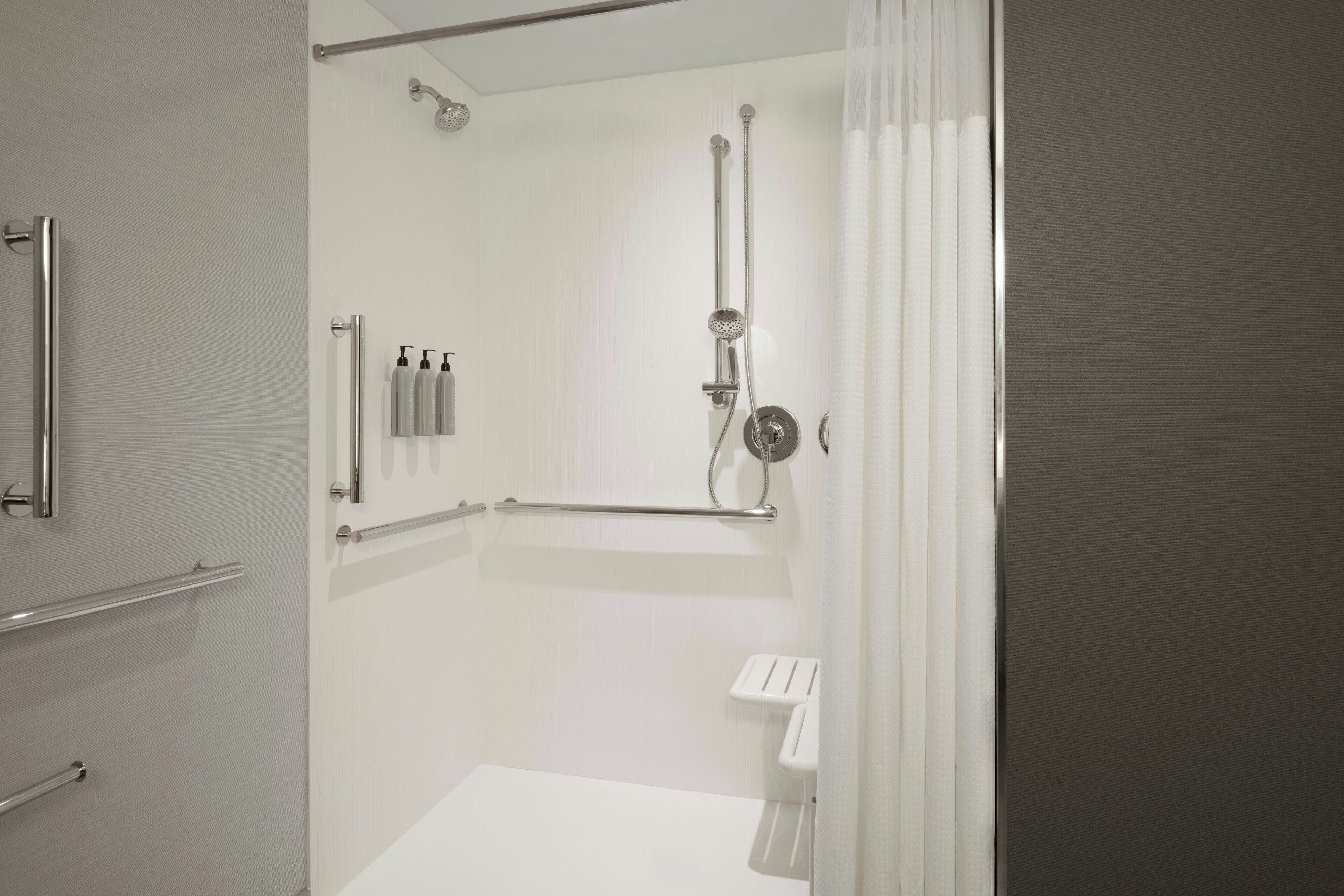 Un bagno moderno con doccia a ingresso facilitato, maniglie di sostegno e lavandino bianco.
