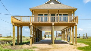 Ein Strandhaus mit zwei Etagen, einem Balkon, Holzstützen und freiem Blick auf den Strand.