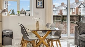 A modern dining area with a glass table and grey chairs, a small plant, and a framed certificate on the wall. - Large 4BR Cowley House, 4 Bath, Sleeps 10 with Parking (Oxford)