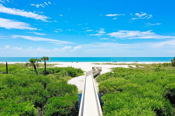 A pathway leading to a beach with clear skies and lush greenery.