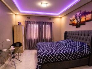 A bedroom with a bed, a desk, a chair, curtains, and a wall-mounted artwork. - Seven Palms Executive Lodge (Ndola)