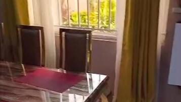 Un comedor con mesa y sillas de cristal, cortinas amarillas y vistas al exterior con vegetación.