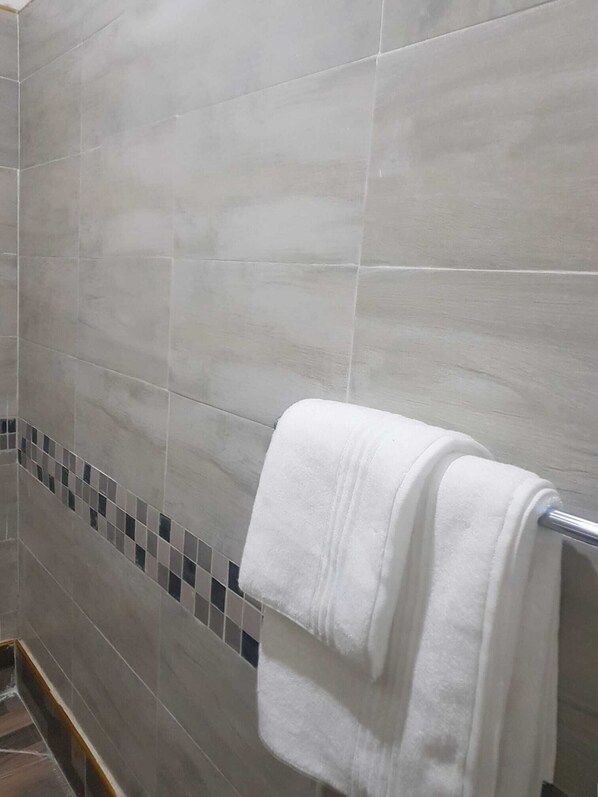 A bathroom with grey tiles, a white towel on a metal towel rack, and a small tiled accent strip. - Seven Palms Executive Lodge (Ndola)