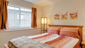 Un lit bien fait, recouvert d’une couvre-lit à rayures, une lampe de chevet et trois tableaux accrochés au mur.