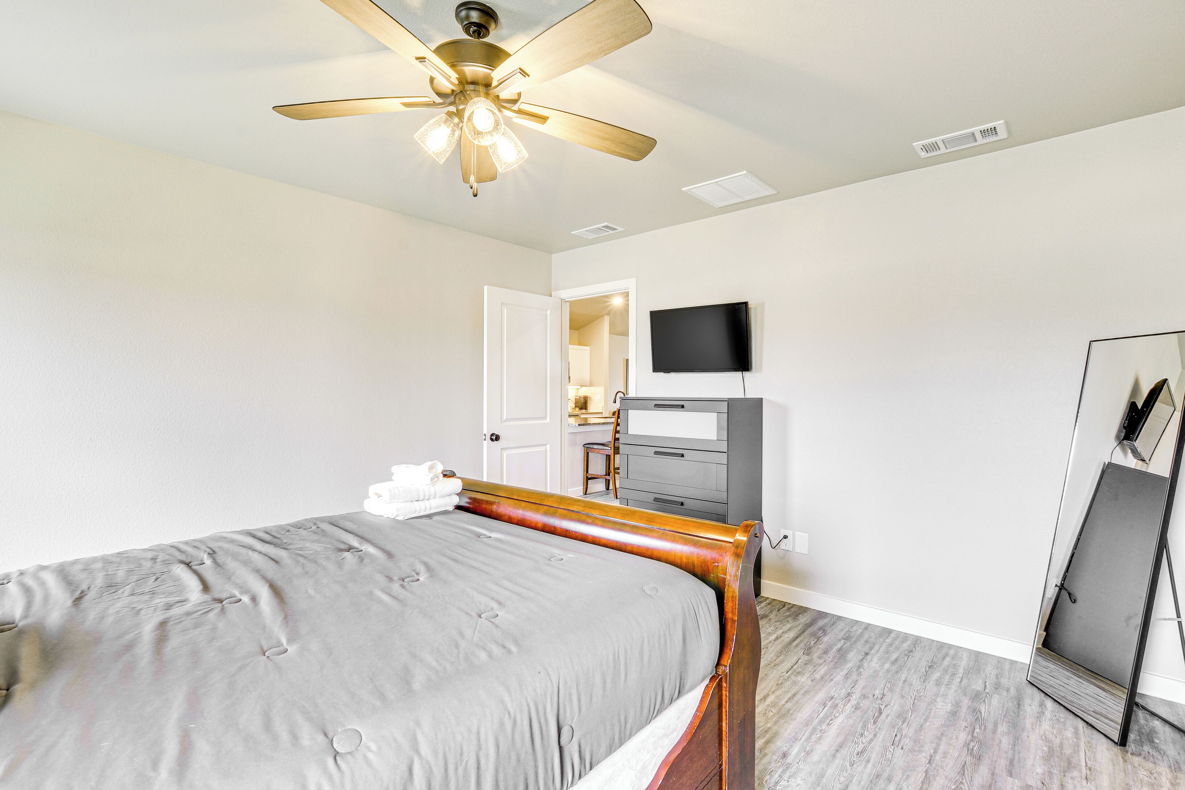 A bedroom with a bed, a ceiling fan, a television, and a mirror.