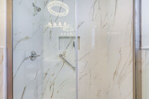 A glass-enclosed shower with a marble wall, a handrail, and a showerhead.