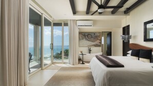 Une chambre d’hôtel moderne avec un grand lit, une vue sur l’océan, un ventilateur de plafond et un tableau au mur.