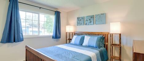 A bedroom with a wooden bed, blue curtains, a window, and two bedside lamps.