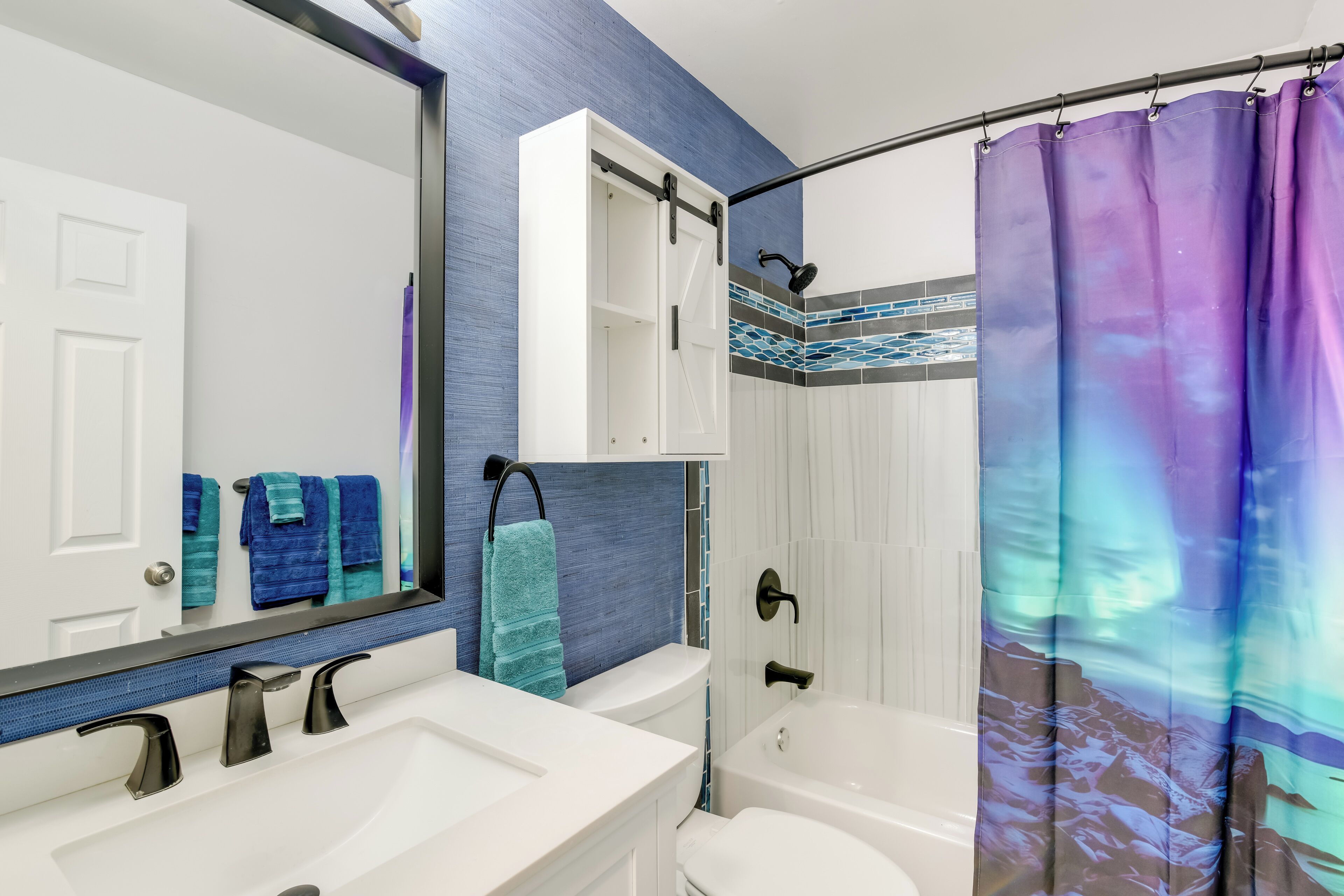 A bathroom with a white sink, a mirror, a white toilet, and a shower with a purple curtain.