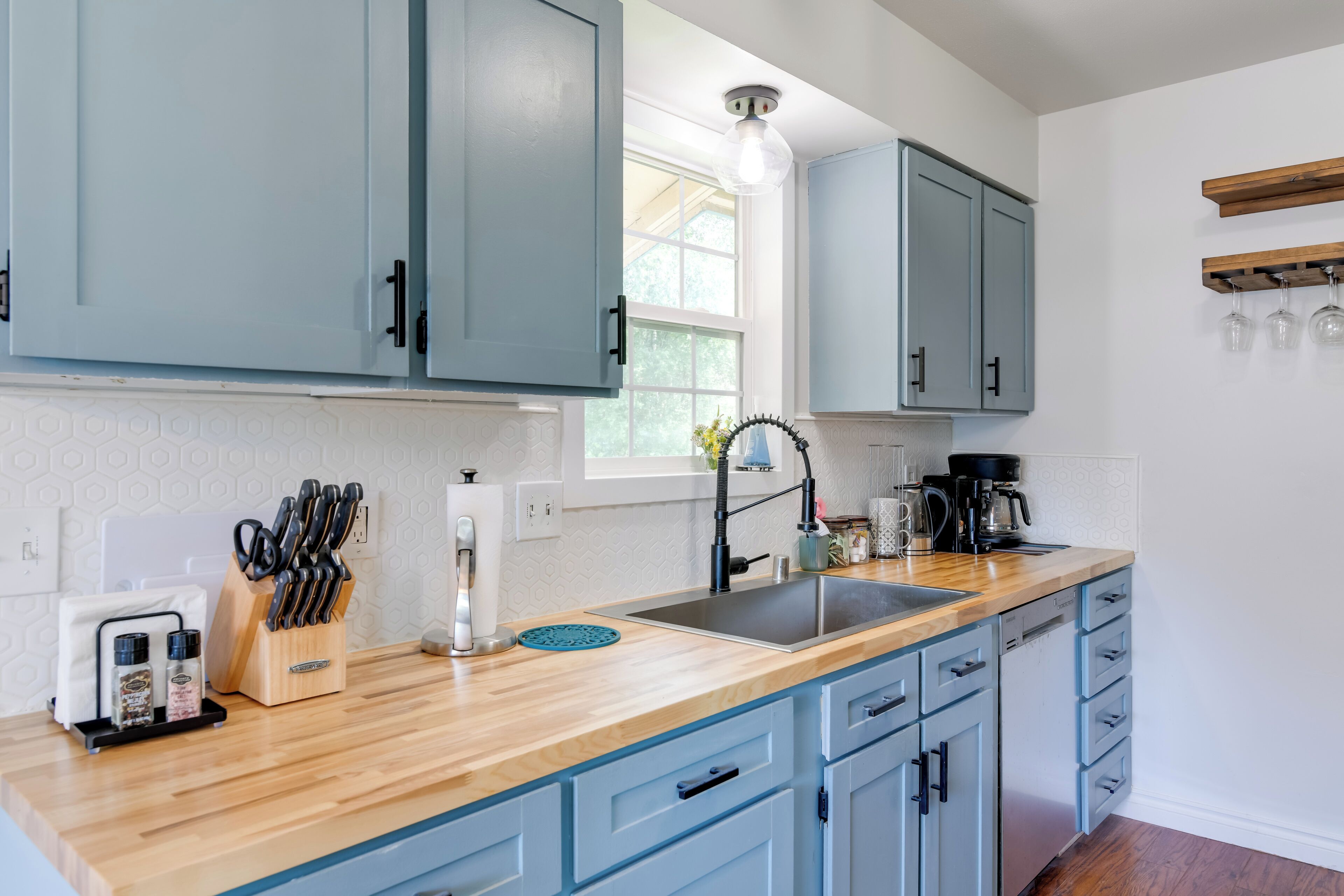 Una cocina con armarios azul claro, encimera de madera, un fregadero y una ventana con luz natural.
