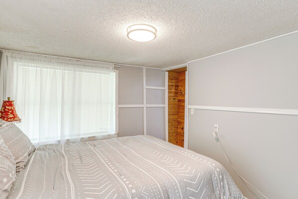 A bedroom with a bed, a window with curtains, a wooden wardrobe, and a ceiling light.