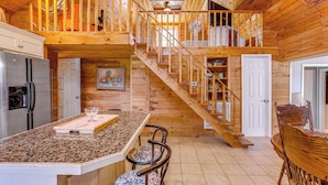 A wooden cabin interior with a kitchen, dining area, and a staircase leading to an upper level. - Greers Ferry Home w/ Fire Pit Near Shiloh Marina! (Higden)