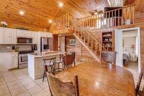 A spacious kitchen with a central island, wooden staircase, and a dining area with a large table and chairs.
