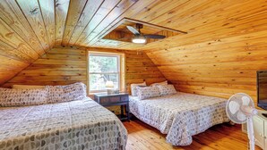 A cozy attic bedroom with wooden walls, two beds with patterned bedding, a ceiling fan, and a window providing natural light. - Greers Ferry Home w/ Fire Pit Near Shiloh Marina! (Higden)