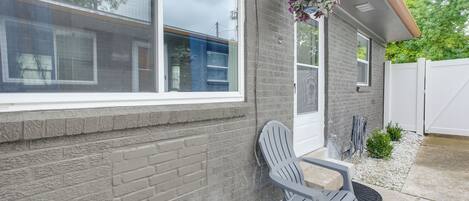 A house with a brick exterior, a window, a gray Adirondack chair, and a hanging flower basket.