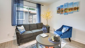 Een woonkamer met een grijze bank, een blauwe fauteuil, een ronde salontafel en een kamerplant.