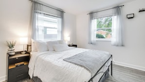 Een slaapkamer met een bed, nachtkastjes, een raam en uitzicht op groen buiten.
