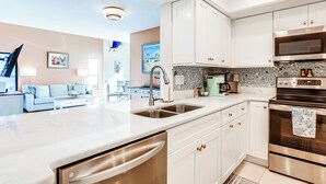 A modern kitchen with white cabinetry, stainless steel appliances, and a large island with a dishwasher. - Key Retreat: Bay Views & Private Beach Access (Englewood)