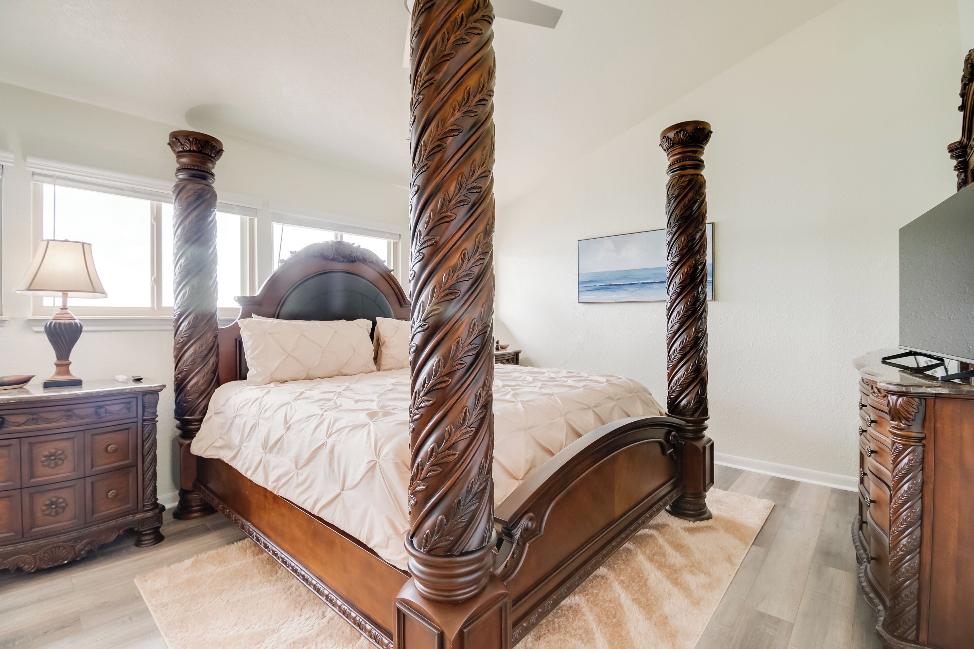 A four-poster bed with intricate woodwork, a nightstand with a lamp, and a dresser with drawers.
