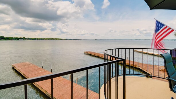 A wooden deck with a railing, a flag, and a view of a body of water. - Lake Conroe Condo: Balcony, Views & Pool Access! (Willis)
