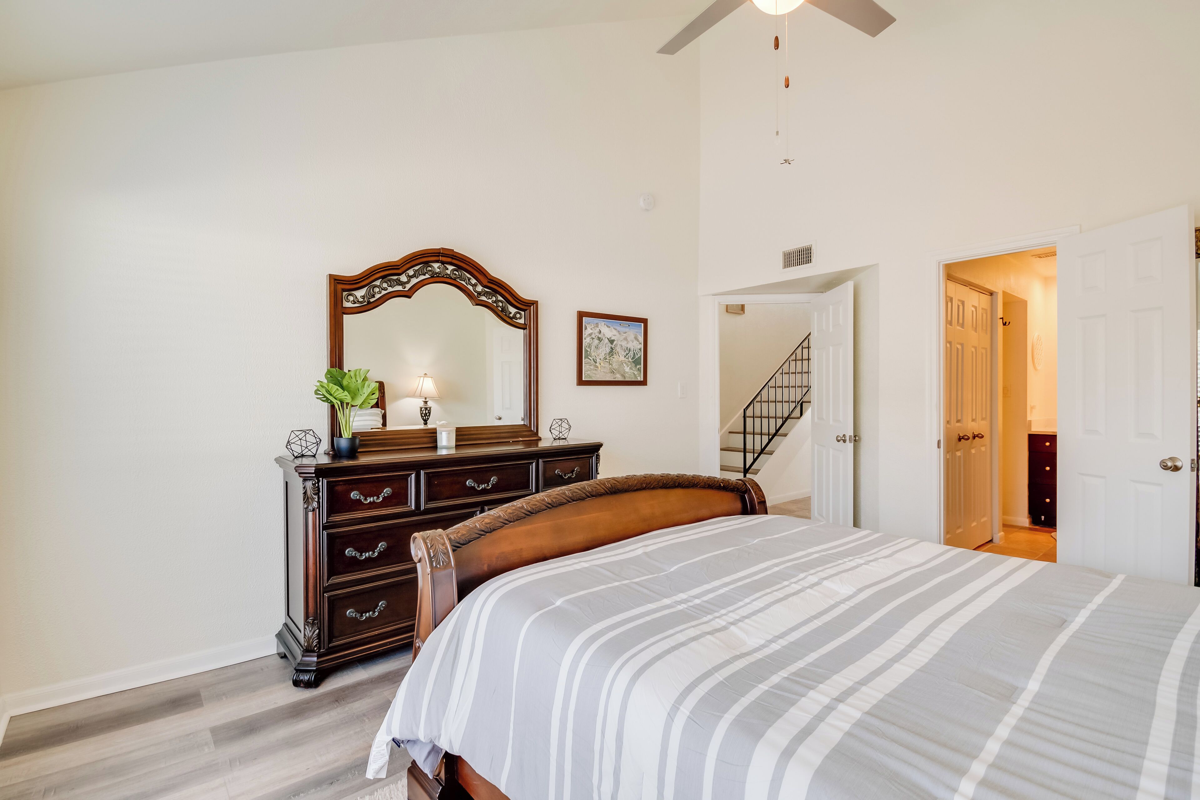 Une chambre à coucher comprenant un lit, une commode, un miroir et un escalier menant à une autre pièce.
