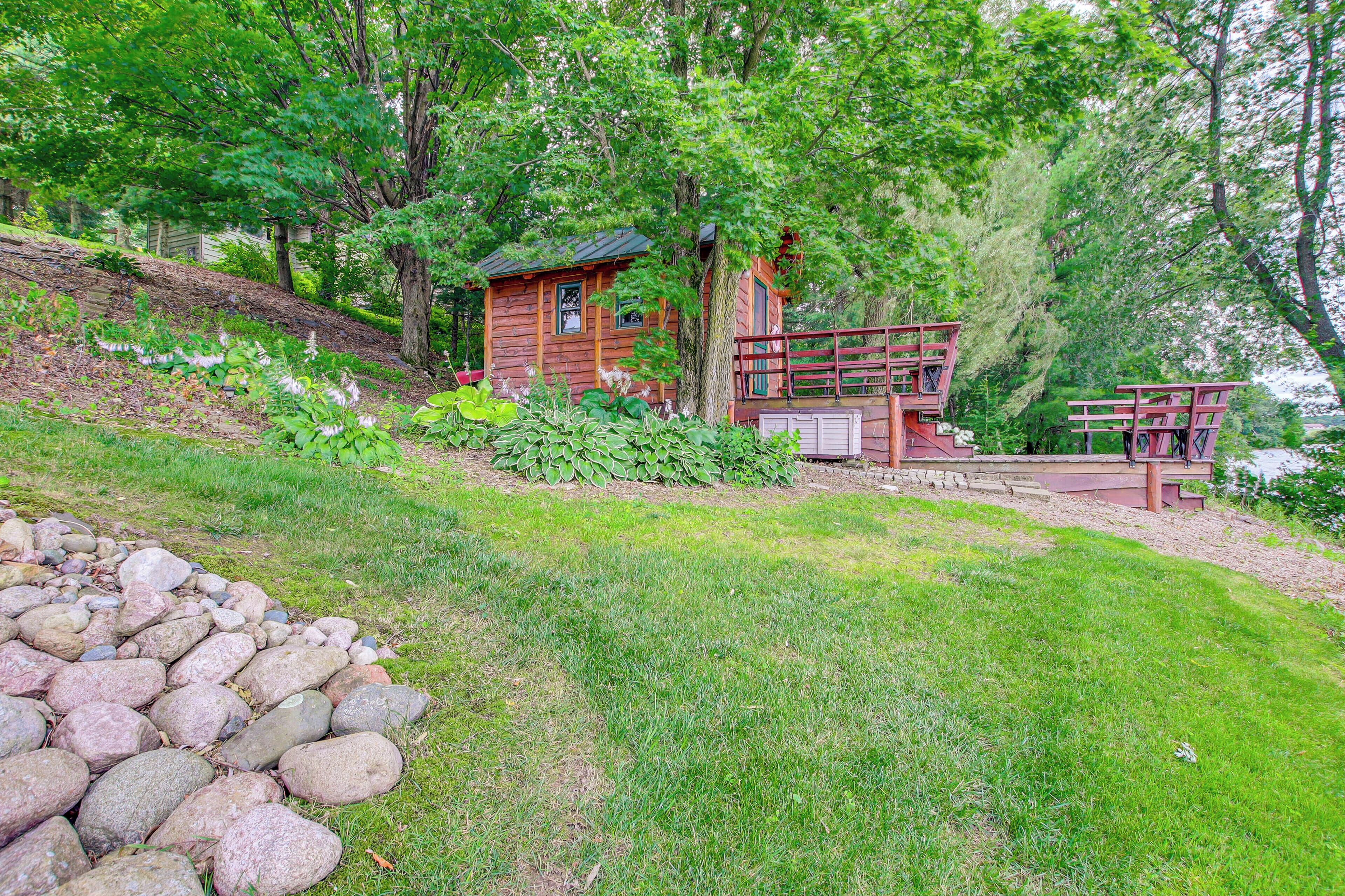A cabin with a deck and a small porch, surrounded by trees and a grassy area.