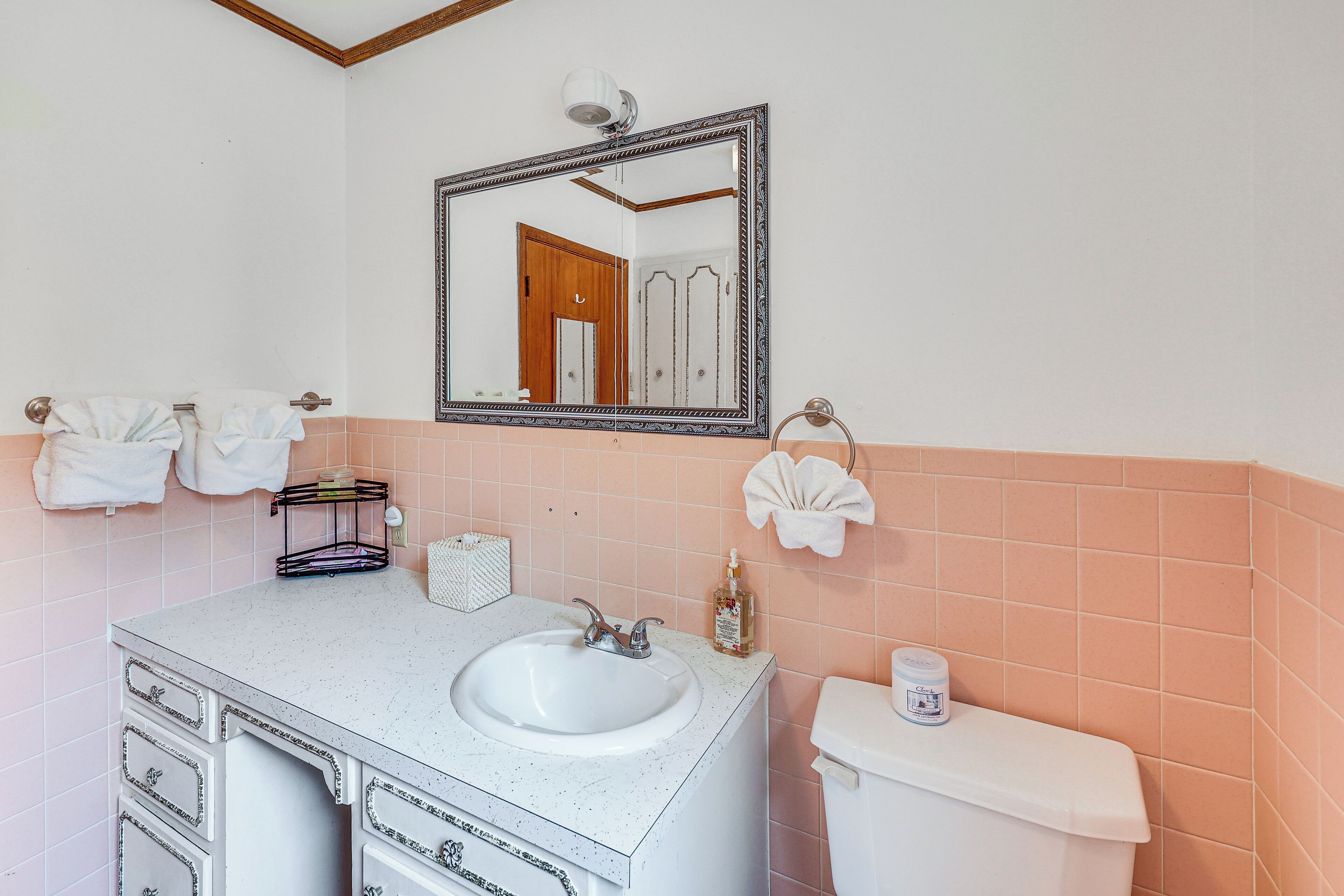 Ein Badezimmer mit weißem Waschbecken, einem Spiegel, einer Toilette und rosa gefliesten Wänden.