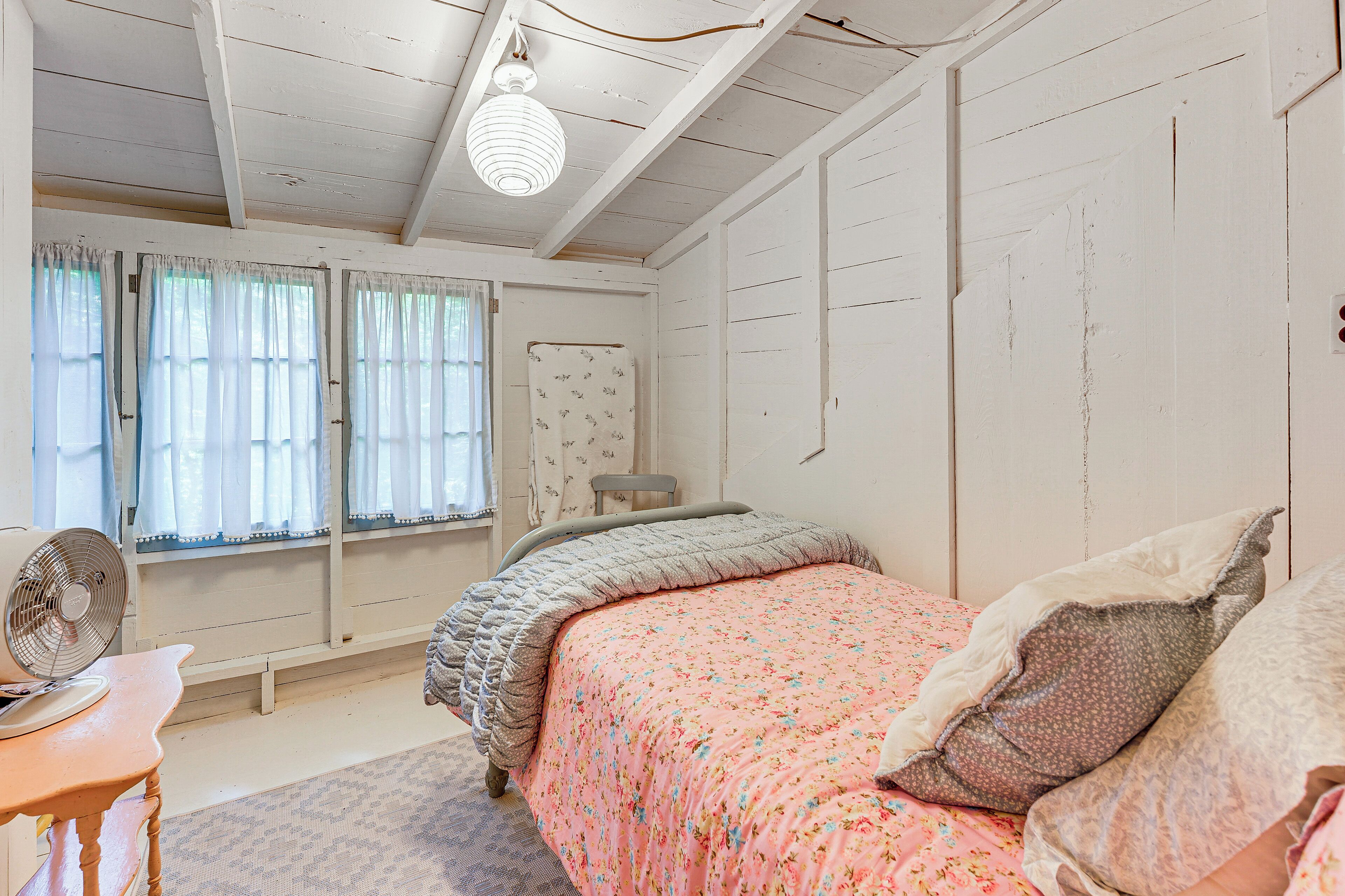 Quarto com cama, ventilador, cadeira e janela com cortinas.