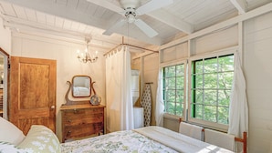 A bedroom with a wooden door, a dresser, a bed with floral bedding, a ceiling fan, and a window with curtains. - ~ 1 Mi to Dtwn Grand Haven: Lake Michigan Cabin (Grand Haven)