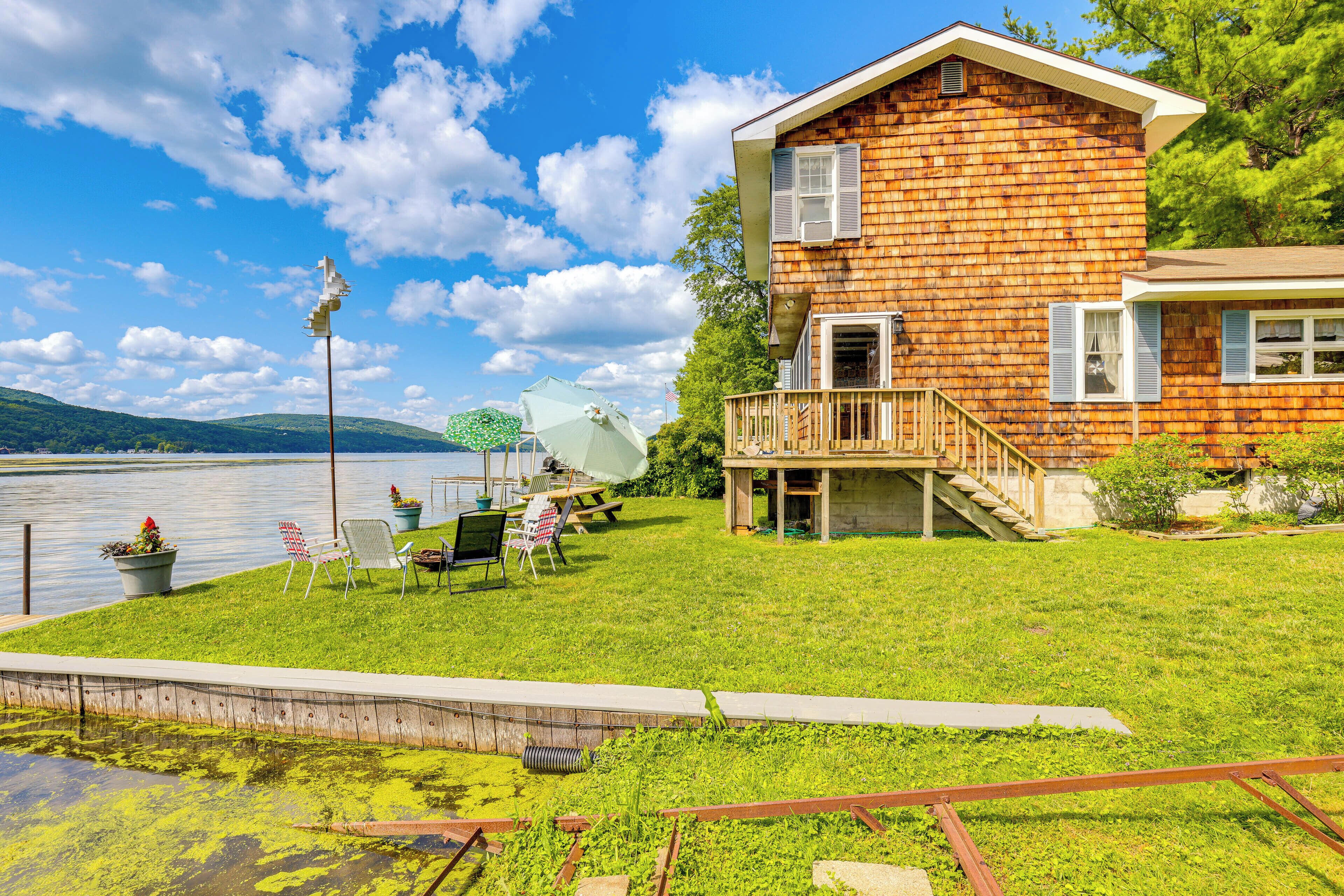 A wooden house with a balcony, a grassy yard, and a lake view.