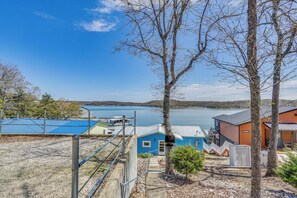 A lakeside property with a blue building, a wooden deck, and a view of the lake. - Shared Dock at Waterfront Lake of the Ozarks Home (Gravois Mills)