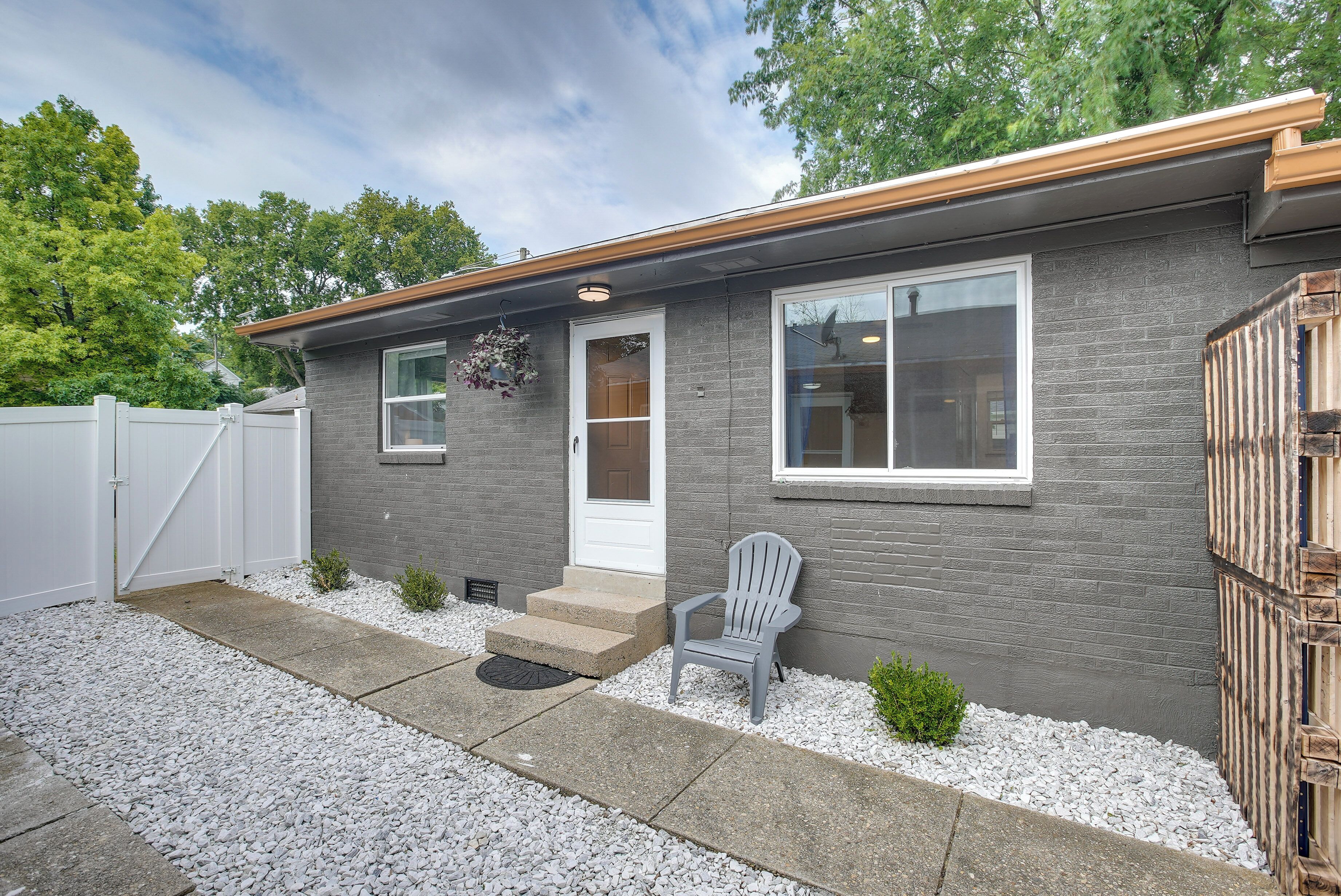 A modern house with a gray brick exterior, a white door, and a gray chair outside.