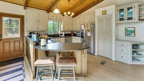 Een keuken met een centraal eiland, houten balken in het plafond, witte kastjes en een koelkast.