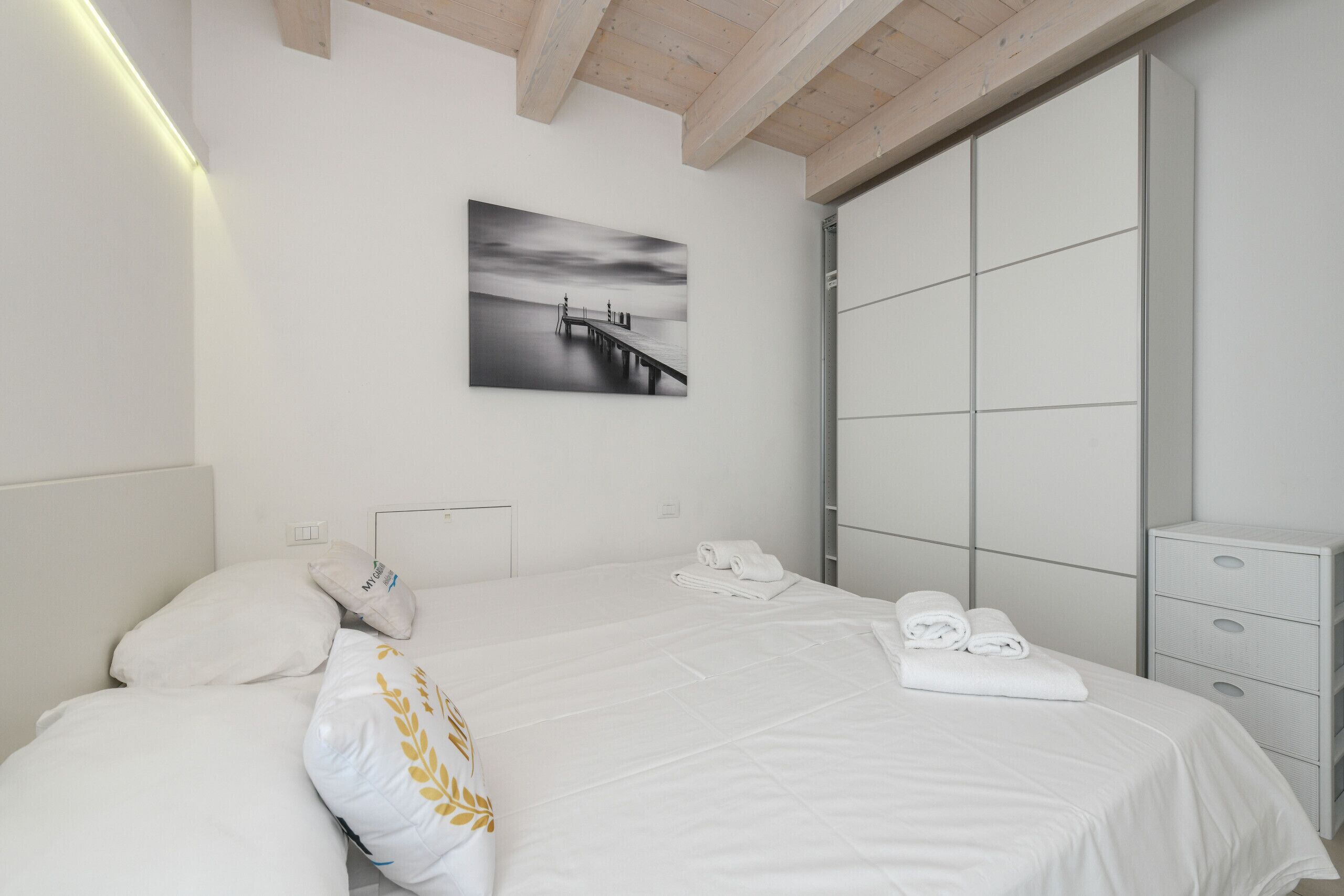 A modern bedroom with a large bed, a nightstand, a wardrobe, and a wall-mounted picture.