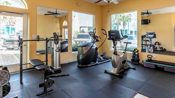 Ein Fitnessraum mit Trainingsgeräten, Deckenventilator und großen Fenstern.