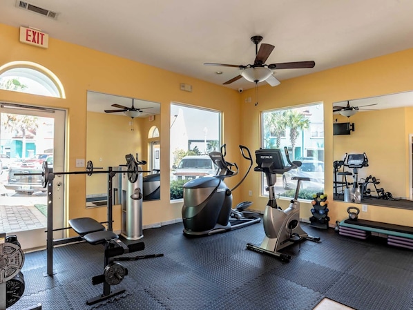 A gym with exercise equipment, a ceiling fan, and large windows.