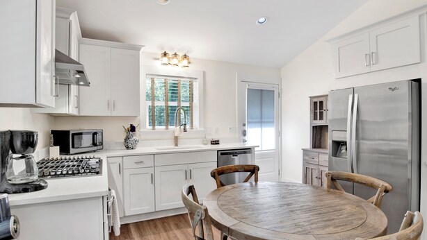 A modern kitchen with white cabinetry, a stainless steel refrigerator, a wooden dining table, and a coffee maker. - NEW LISTING! Peaceful, Fairhope Cottage (Fairhope)