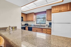 A kitchen with granite countertops, wooden cabinets, a built-in dishwasher, and a refrigerator. - E-131 -Walk From Lanai to Pool and More (Naples)
