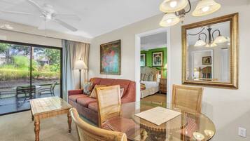 A room with a glass dining table, wicker chairs, a red sofa, a ceiling fan, and a large mirror.