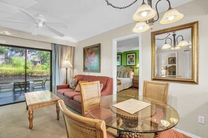 Une pièce avec une table à manger en verre, des chaises en osier, un canapé rouge, un ventilateur de plafond et un grand miroir.