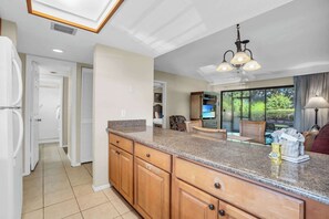 A kitchen with wooden cabinets, a granite countertop, and a built-in oven. There is a large window with a view of greenery outside.