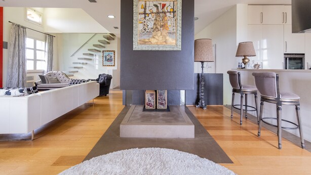 A modern living room with a sofa, a fireplace, a dining area with bar stools, and a kitchen in the background.