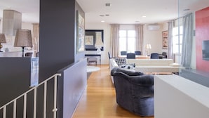 A modern living room with a sofa, a dining area, and a kitchen visible in the background.