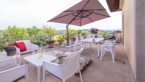 An outdoor patio with white wicker furniture, a large umbrella, and potted plants.